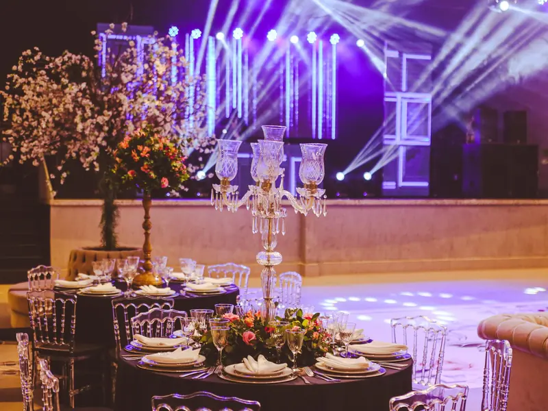 Round tables laid for a gala dinner, with a crystal candelabra and a lit stage behind