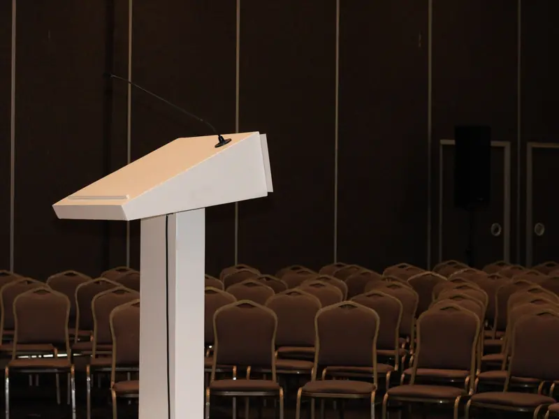 Speaker's lectern with a microphone in front of rows of empty chairs in a conference room